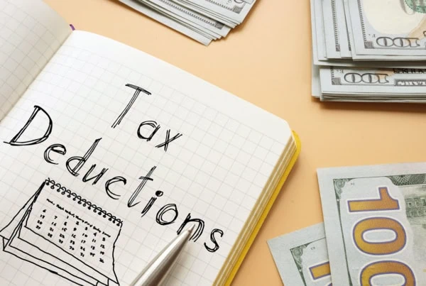 the words tax deductions are written on a notepad sitting on a table with many hundred dollar bills.