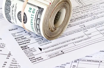 a roll of hundred dollar bills sits on a tax return.