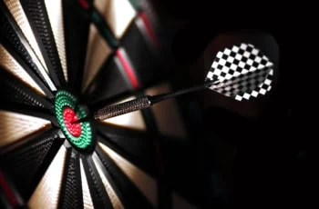 One arrow in the center of a dartboard in a darkly lit space.