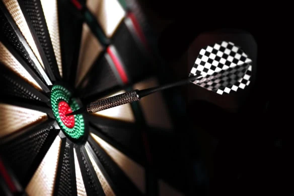 One arrow in the center of a dartboard in a darkly lit space.