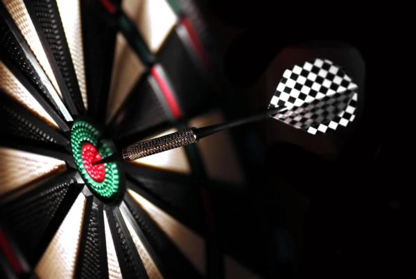 One arrow in the center of a dartboard in a darkly lit space.
