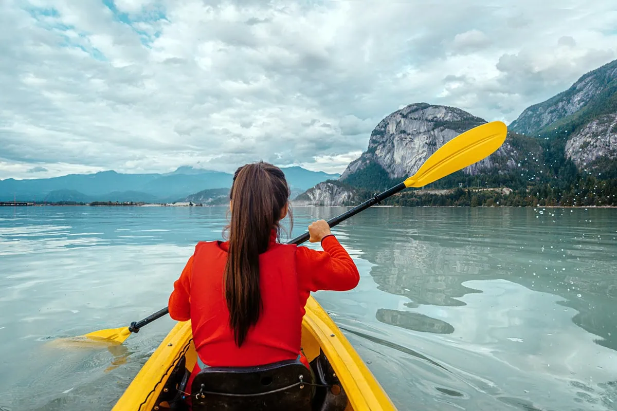 a woman kayaks in Howe Sound in a calm fjord.