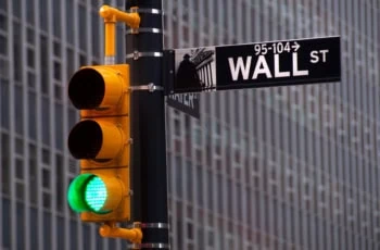 a wall street street sign in the foreground and a traffic signal lit green in the background.