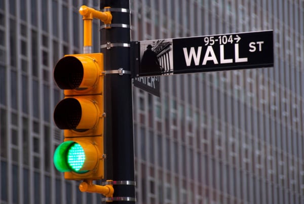 a wall street street sign in the foreground and a traffic signal lit green in the background.