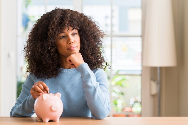 woman putting money in a piggy bank thinking