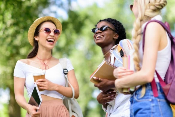 young female students laughing holding books and tablet