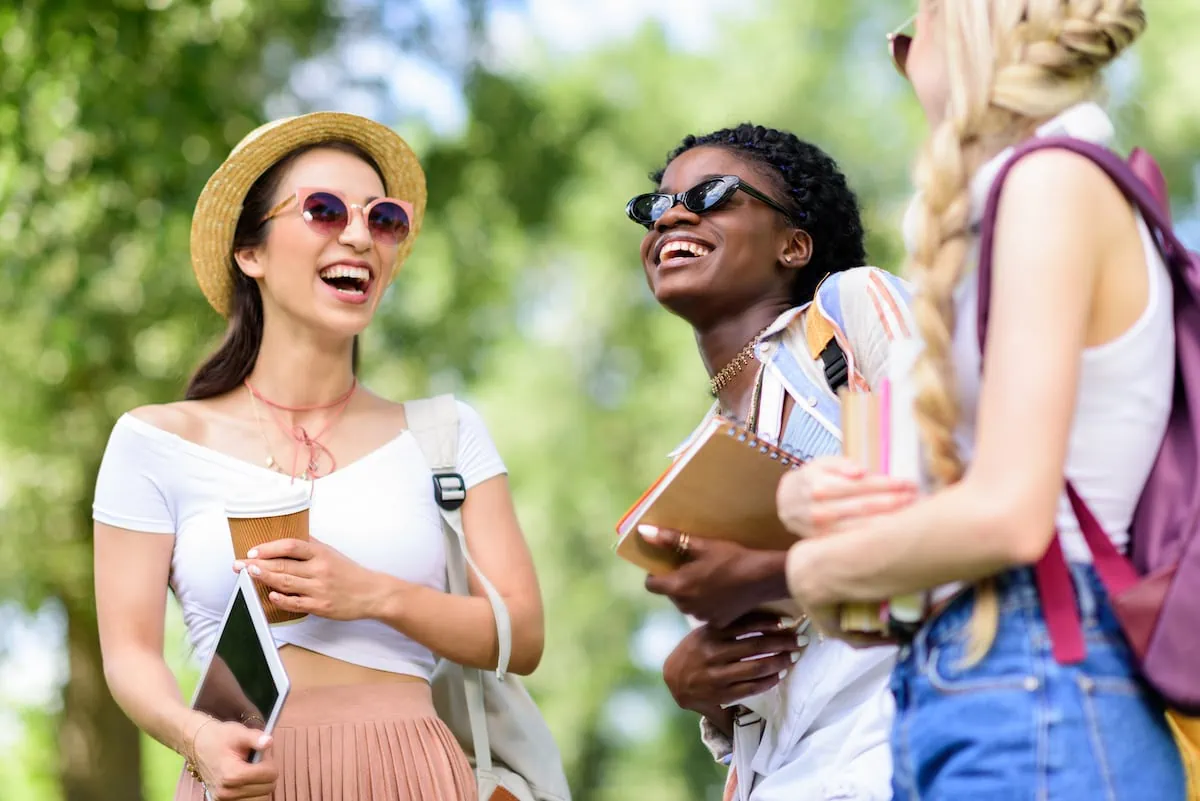 young female students laughing holding books and tablet