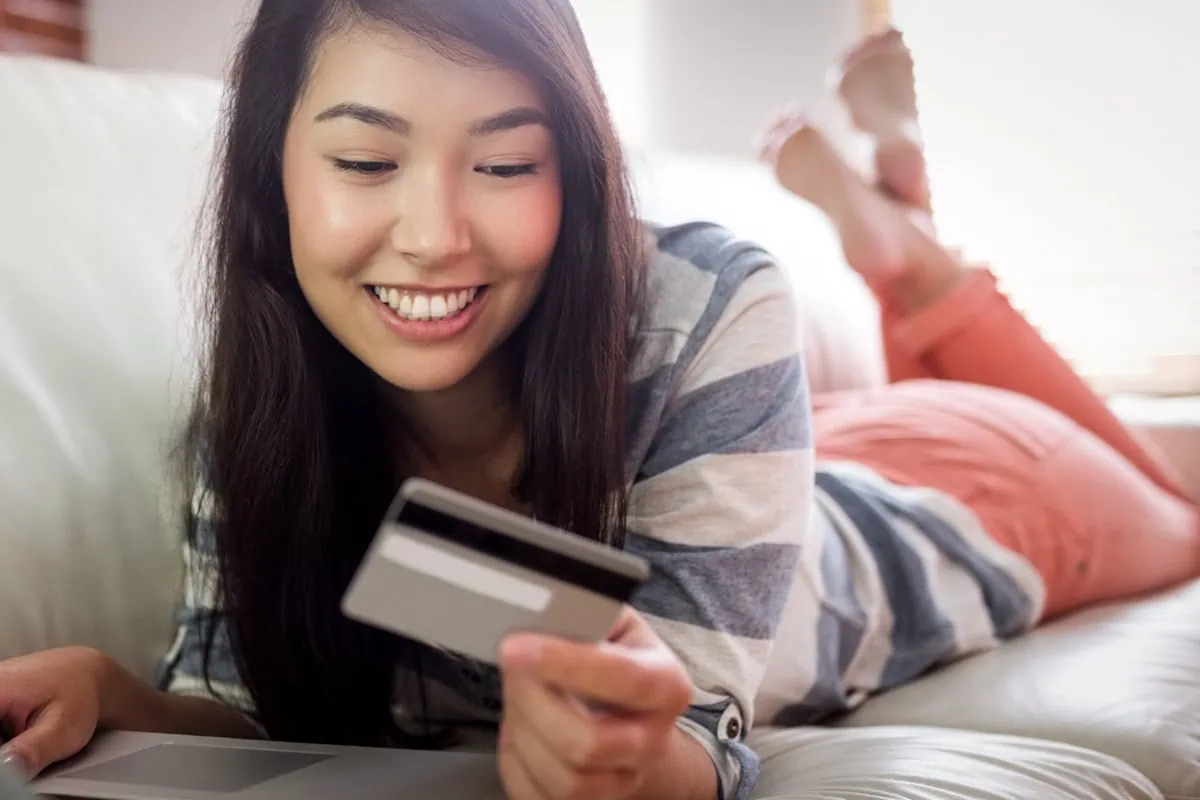 Safety Net Included: 7 Free Debit Cards That Give Kids Freedom (and Parents Control) 35 A young woman is on the couch looking at a debit card.